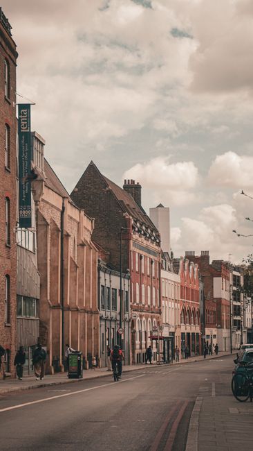 A street scene in Hounslow showing a row of multi-storey buildings with varying architectural styles, including brick facades, some with large windows and decorative elements. On the pavement, there a